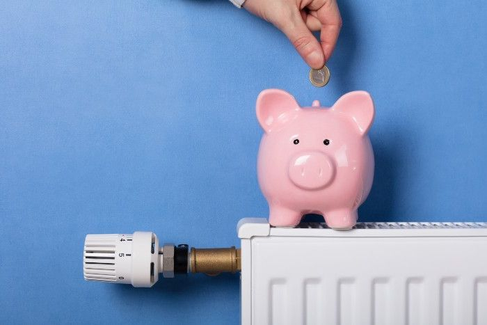 Hand wirft Geld in Sparschwein auf Heizung